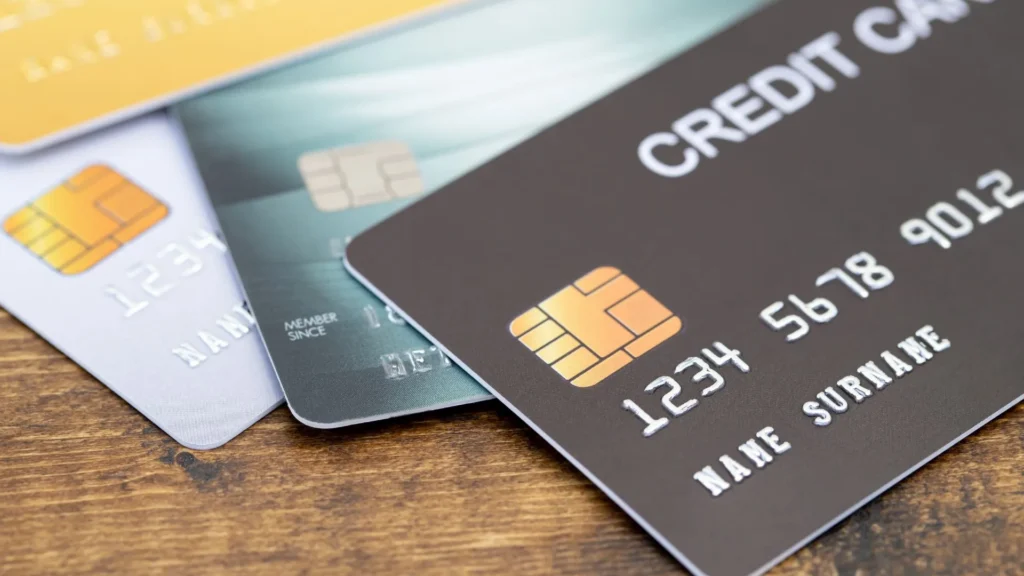 A close-up image of multiple credit cards on a wooden surface, showcasing their chip and embossed details.